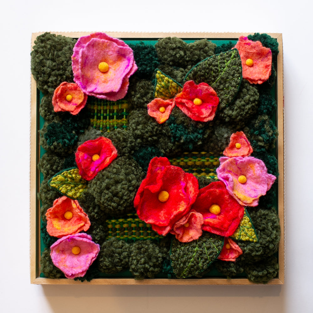 Mossy green pom pom sculpture covered in weavings and red and pink flowers.